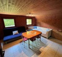 NA PREDAJ Chata na Duchonke- Prašice - Izba v chate s dreveným obkladom, sedačkou a stolom s jedálenskými stoličkami.