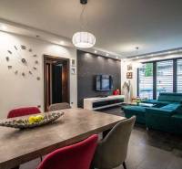 Priestranný 5-izbový rodinný dom s pohodlným dojazdom do Bratislavy  - Obývačka rodinného domu s komfortnou sedačkou, stolíkom a televízorom, veľké okná vpúšťajú svetlo.