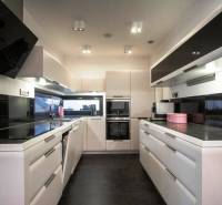 Priestranný 5-izbový rodinný dom s pohodlným dojazdom do Bratislavy  - Kuchyňa v rodinnom dome s čiernymi spotrebičmi, bielymi skrinkami a tmavou dlažbou.