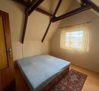 PREDAJ - Zrekonštruovaná rekreačná chata - Chľaba - Spálňa s dreveným dekórom, strešné trámy, jednoduché zariadenie, posteľ, koberček, záclona.