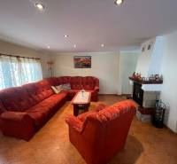 PREDAJ - Zrekonštruovaná rekreačná chata - Chľaba - Obývacia izba s krbom, červeným gaučom a podlahou s dreveným dekorom v chate.