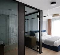 Prenájom 2-izbový byt s loggiou,55m2, EUROVEA TOWER - Spálňa s presklenou kúpeľňou, posteľou a podlahou s dreveným dekorom v 2-izbovom byte.