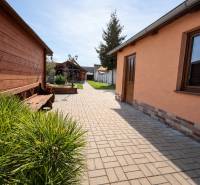 Rodinný dom s terasou, garáž, pozemok 902m2, Dojč, okr. Senica - Dvor rodinného domu v Dojči s lavičkou, záhradou a dlaždeným chodníkom.