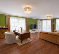 Rodinný dom s terasou, garáž, pozemok 902m2, Dojč, okr. Senica - Obývacia izba s podlahou s dreveným dekorom, zelenou stenou a pohodlnou sedačkou v rodinnom dome.