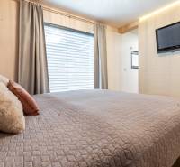 NA PREDAJ SMART 4-IZB BUNGALOV SO ZÁHRADOU A VÝHĽADOM NA JAZERO - Spálňa s veľkou posteľou, závesmi, obrazovkou na stene a dekoratívnymi vankúšmi v rodinnom dome.