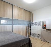 NA PREDAJ SMART 4-IZB BUNGALOV SO ZÁHRADOU A VÝHĽADOM NA JAZERO - Spálňa v rodinnom dome s podlahou s dreveným dekorom, úložnými skriňami a posteľou.