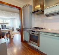 Predaj, 4izbový byt  Fončorda, Banská Bystrica - Kuchyňa s plynovým sporákom a obývačka v 4-izbovom byte, podlaha s dreveným dekorom.