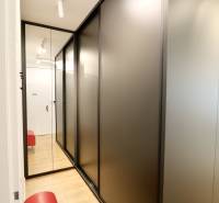 Komfortne vybavený 2-izbový byt v projekte 2 Sýpky - Chodba s čiernymi skriňami, zrkadlom a podlahou s dreveným dekorom v 2-izbovom byte.