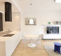 Komfortne vybavený 2-izbový byt v projekte 2 Sýpky - Obývacia izba v 2-izbovom byte s kuchyňou, jedálenským stolom a podlahou s dreveným dekorom.