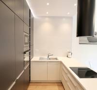 Komfortne vybavený 2-izbový byt v projekte 2 Sýpky - Kuchyňa s tmavými skriňami, bielou linkou a podlahou s dreveným dekorom v 2-izbovom byte.