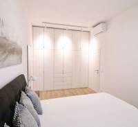 Komfortne vybavený 2-izbový byt v projekte 2 Sýpky - Svetlá spálňa s bielou vstavanou skriňou a podlahou s dreveným dekorom v 2-izbovom byte.