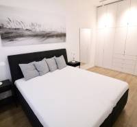 Komfortne vybavený 2-izbový byt v projekte 2 Sýpky - Spálňa v 2-izbovom byte s bielymi skriňami a podlahou s dreveným dekorom.