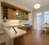 Predaj 4+1 izbový byt, 110 m2, 2 balkóny, Obchodná ul, centrum BA - Kuchyňa v 4-izbovom byte s podlahou s dreveným dekorom, bielym nábytkom a rastlinami.