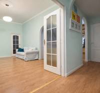 Predaj 4+1 izbový byt, 110 m2, 2 balkóny, Obchodná ul, centrum BA - Izba v 4-izbovom byte s podlahou s dreveným dekorom, bledé steny, pohodlné kreslo.