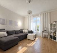 Predaj 4+1 izbový byt, 110 m2, 2 balkóny, Obchodná ul, centrum BA - Svetlá obývačka v 4-izbovom byte s podlahou s dreveným dekorom, sivou pohovkou a bielym nábytkom.