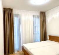 I 3 i byt s parkovaním v rezidenčnom komplexe METROPOLIS - Spálňa s posteľou v 3-izbovom byte, posteľ s dreveným dekorom a závesmi.