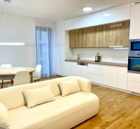 I 3 i byt s parkovaním v rezidenčnom komplexe METROPOLIS - Obývacia izba s kuchyňou v 3-izbovom byte, podlaha s dreveným dekorom, biele zariadenie.