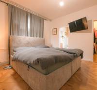 Na predaj zrekonštruovaný dom na Štefánikovej ulici, Trenčín - Spálňa v rodinnom dome s posteľou, závesmi, TV a podlahou s dreveným dekorom.