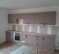 PREDAJ – 4-izbový rodinný dom v radovej zástavbe s garážou - Kuchyňa v rodinnom dome s podlahou s dreveným dekorom a šedými skrinkami.