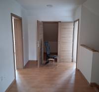 PREDAJ – 4-izbový rodinný dom v radovej zástavbe s garážou - Izba v rodinnom dome s podlahou s dreveným dekorom a tromi drevenými dverami.