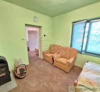 Pôvodný domček v obci Nová Vieska - Izba v rodinnom dome s kachľami, dvoma kreslami a podlahou s dreveným dekorom.