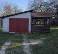 Rodinný dom s pozemkom 1978 m2  v  lokalite – Prašice. - Rodinný dom v Prašiciach s prístreškom a veľkými červenými dverami na záhrade.