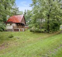 NA PREDAJ CHATA V REKREAČNEJ OBLASTI RUDAVA, OBEC MALÉ LEVÁRE - Chata v Malých Levároch obklopená zeleňou s červenou plechovou strechou a trávnatou cestou.