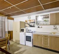 NA PREDAJ CHATA V REKREAČNEJ OBLASTI RUDAVA, OBEC MALÉ LEVÁRE - Kuchyňa chaty s oknom a kuchynskou linkou, pričom stôl má kvetinovú výzdobu.