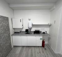 Prenájom ordinácie v zdravotnom stredisku Saratovská 24, Bratislava. - Interiér obchodných priestorov s kuchynským kútom, umývadlom a protipožiarnym vybavením na podlahe s dreveným dekorom.