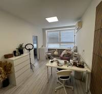 Prenájom ordinácie v zdravotnom stredisku Saratovská 24, Bratislava. - Biela miestnosť s pracovným stolom, lampami a dekoráciou na podlahe s dreveným dekorom.