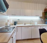 RADO I 2-izbový byt 49m² s terasou 71m² I Soblahov - Kuchyňa v 2-izbovom byte s dreveným dekorom a bielymi skrinkami.