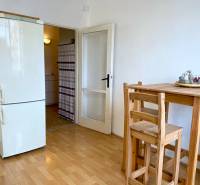 PRENÁJOM 1 izbový byt, 40 M2, Bratislava, Ružinov, Košická ulica, NIVY - Kuchyňa v 1-izbovom byte s dreveným stolom, stoličkami a chladničkou, podlaha s dreveným dekorom.