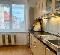 PRENÁJOM 1 izbový byt, 40 M2, Bratislava, Ružinov, Košická ulica, NIVY - Kuchynská linka v 1-izbovom byte s podlahou s dreveným dekorom a výhľadom z okna.