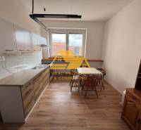 Prenajmem 1 izbový byt v Nových Zámkoch - Kuchyňa v 1-izbovom byte so stolom, stoličkami a podlahou s dreveným dekorom.