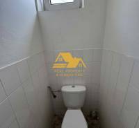 Prenajmem garsónku v Nesvadoch - Kompaktná toaleta s oknom, biele dlaždice, podlaha s dreveným dekorom.