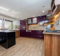 2-Generačný 9izb. RD s bazénom a veľkým pozemkom, Dvorníky - Kuchyňa v rodinnom dome s lesklými fialovými skrinkami a podlahou s dreveným dekorom.
