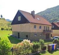 Veľkorysý 10-árový pozemok, slnečná nehnuteľnosť, priestranné bývanie  - Rodinný dom v Liptovských Revúcach s červenou strechou, záhradou a kvetinovým plotom.