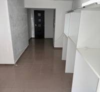 Obchodný priestor, kancelária Sarartovská ul.  - Interiér obchodných priestorov s policami, dvermi a sivou podlahou s lesklým povrchom.