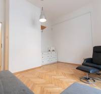 Priestranný 4-izbový byt s predzáhradkou, Staré Mesto - Interiér 4-izbového bytu s kreslom, bielou komodou a podlahou s dreveným dekorom.