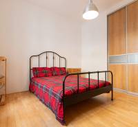 Priestranný 4-izbový byt s predzáhradkou, Staré Mesto - Spálňa v 4-izbovom byte s kovovou posteľou, šatníkovou skriňou a podlahou s dreveným dekorom.