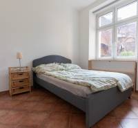 Priestranný 4-izbový byt s predzáhradkou, Staré Mesto - Spálňa v 4-izbovom byte s posteľou, nočným stolíkom a veľkým oknom.