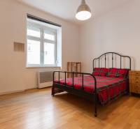 Priestranný 4-izbový byt s predzáhradkou, Staré Mesto - Spálňa v 4-izbovom byte s posteľou, nočnými stolíkmi a podlahou s dreveným dekorom.