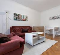 2-izbový byt s balkónom, Ružinov – Ostredky - Obývačka 2-izbového bytu s bordovým gaučom, bielym stolíkom na podlahe s dreveným dekorom.