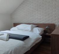 Predaj !Elegantný byt s wellness prvkami pri Jasnej - Spálňa v 2-izbovom byte s posteľou, lampou a tehlovým obkladom na stene.