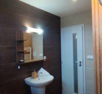 Predaj !Elegantný byt s wellness prvkami pri Jasnej - Kúpeľňa v 2-izbovom byte s tmavými obkladmi, zrkadlom a bielou umývadlovou skrinkou.