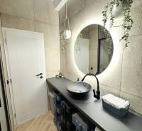 - PRENÁJOM - 3 IZBOVÝ BYT - WILSONOVA UL. - STARÉ MESTO - Kúpeľňa s oblým zrkadlom, závesnými kvetmi a podlahou s dreveným dekorom.