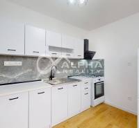 Prenájom 1 izbový byt s loggiou, centrum, Spišská Nová Ves - Kuchyňa v 1-izbovom byte s bielym nábytkom a podlahou s dreveným dekorom.