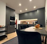 KOMPLETNE prerobený 4i byt s balkónom, 77m2 - ZÁTVOR - Kuchyňa v 4-izbovom byte s podlahou s dreveným dekorom, čiernymi skriňami a jedálenským stolom.