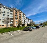 Na prenájom slnečný 2i byt s balkónom, ul. Východná, Trenčín - Bytovka na ulici Východná, parkovisko, stromy, 2-izbový byt, modrá obloha, auto.