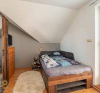 Predaj priestranného rodinného domu v historickej časti Popradu  - Spálňa v rodinnom dome s útulnou posteľou, šikmým stropom a podlahou s dreveným dekorom.